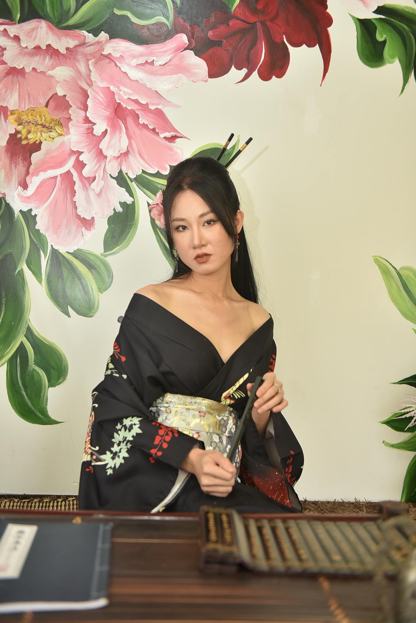 A woman in a traditional Japanese kimono posing gracefully indoors with floral wallpaper.